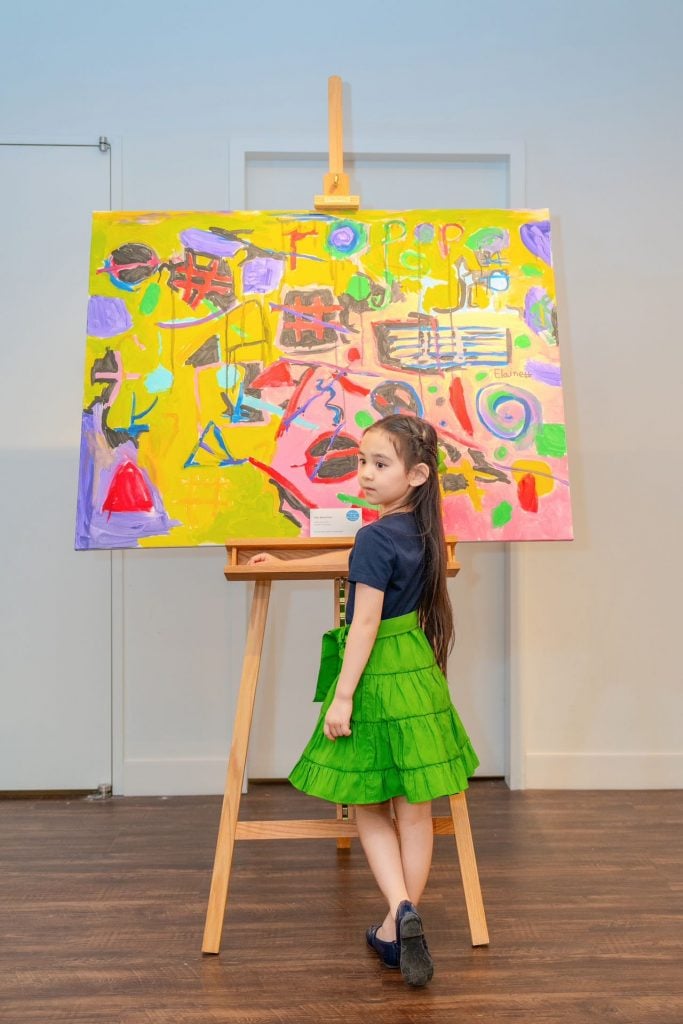 Photo of Elaine Fan standing in front of one of her bright yellow abstract paintings that is on a full-size easel.