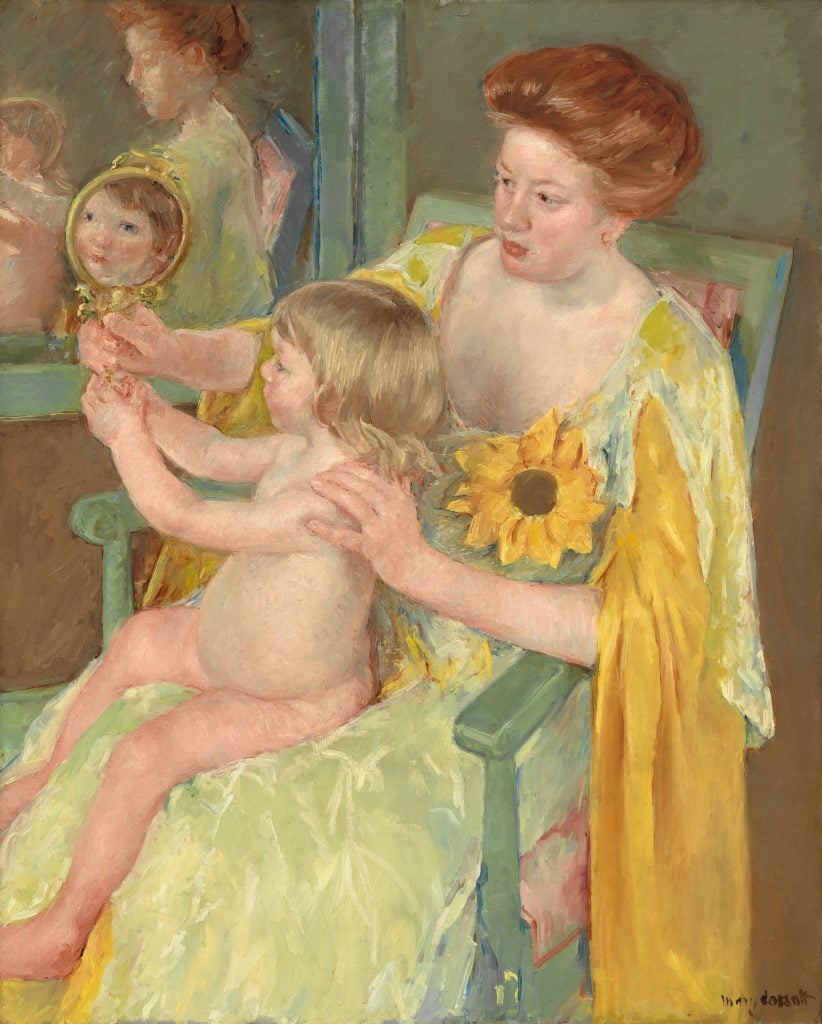 a woman sits in a chair holding a child with a sunflower pinned to her breast